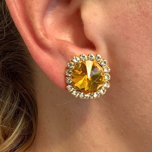 May include: A pair of gold tone earrings with a large amber colored crystal surrounded by a halo of clear rhinestones.