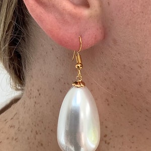 May include: A pair of gold tone earrings with a large, white, pearlescent teardrop-shaped pendant.