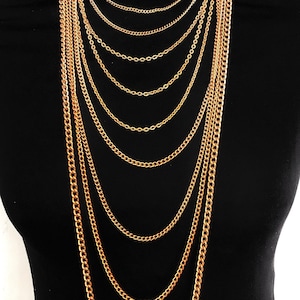 May include: A gold layered chain necklace with multiple links of varying sizes. The necklace is displayed on a black mannequin.