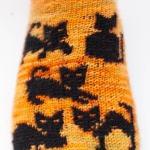 Könnte beinhalten: Orangefarbene und gelbe Stricksocke mit einem schwarzen Katzenmuster.
