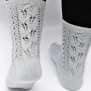 Könnte beinhalten: Ein Paar hellgraue Stricksocken mit einem zarten Spitzenmuster. Die Socken sind knöchelhoch und haben eine bequeme Passform.