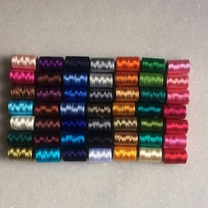 May include: A collection of colorful spools of thread, arranged in neat rows. The threads are in a variety of colors, including pink, purple, blue, silver, orange, green, and red. The spools are tightly wound and appear to be made of a shiny material.