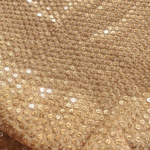 Puede incluir: Primer plano de una tela dorada con un patrón repetitivo de pequeñas lentejuelas redondas.