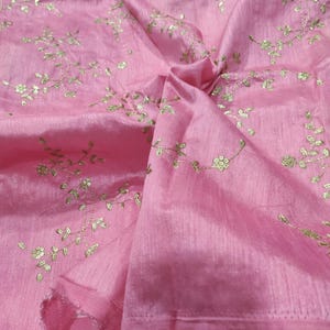 Könnte beinhalten: Rosa Stoff mit goldener Blumenstickerei. Der Stoff hat einen subtilen Glanz. Die goldene Stickerei zeigt zarte Blumen- und Blattmuster, die ein elegantes und detailliertes Design ergeben.
