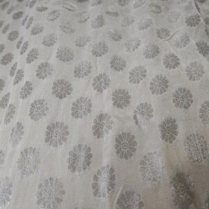 May include: White fabric with a repeating pattern of silver floral designs.