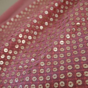 May include: Pink fabric with a pattern of small, round, gold sequins.