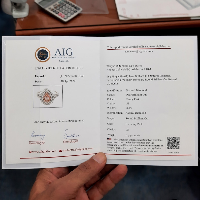 以下が含まれることがあります： AIG GemLabのジュエリー鑑定書。洋梨型ブリリアントカットの天然ダイヤモンド、ファンシーピンクカラー、ラウンドブリリアントカットダイヤモンドのリングの詳細が記載されています。重量、クラリティ、その他の仕様が含まれています。