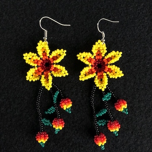 May include: A pair of beaded earrings featuring yellow and orange flower designs. The earrings have a black beaded stem with red, yellow, and green beaded accents. The earrings hang from silver-colored hooks.
