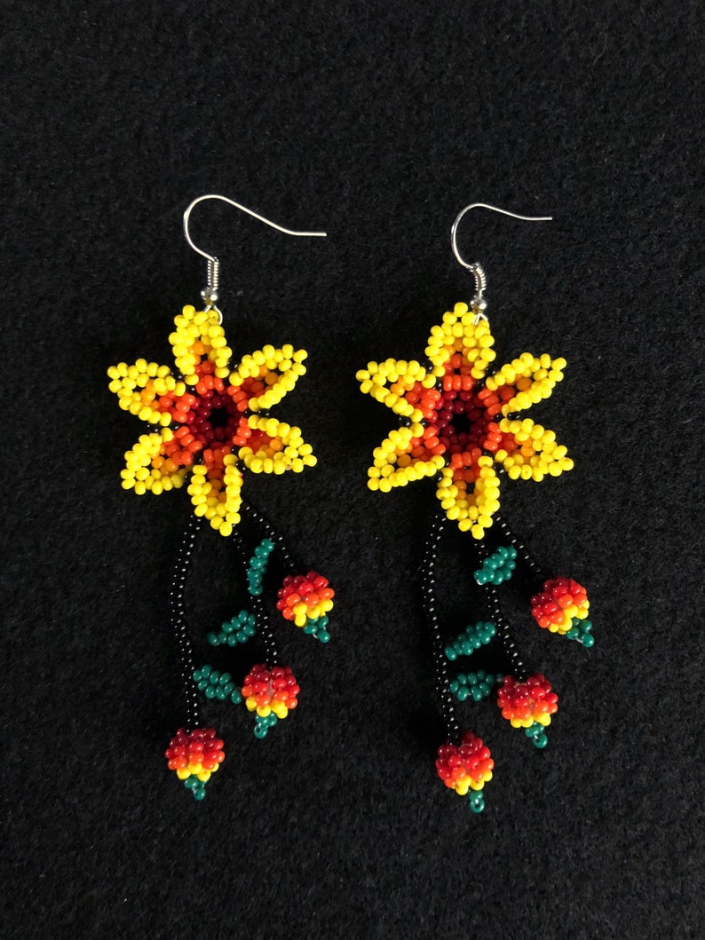 May include: A pair of beaded earrings featuring yellow and orange flower designs. The earrings have a black beaded stem with red, yellow, and green beaded accents. The earrings hang from silver-colored hooks.