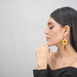 May include: A pair of vibrant, handmade earrings featuring a yellow flower design with red and green accents. The earrings dangle with beaded strands in shades of red, green, and yellow, creating a striking floral accessory.