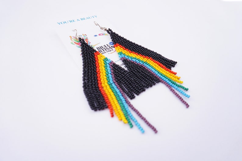 May include: A pair of beaded earrings with a black top section and rainbow fringe. The earrings are on a white card with the text "YOU'RE A BEAUTY" and the logo "BIJOU ARTISAN BOUTIQUE".