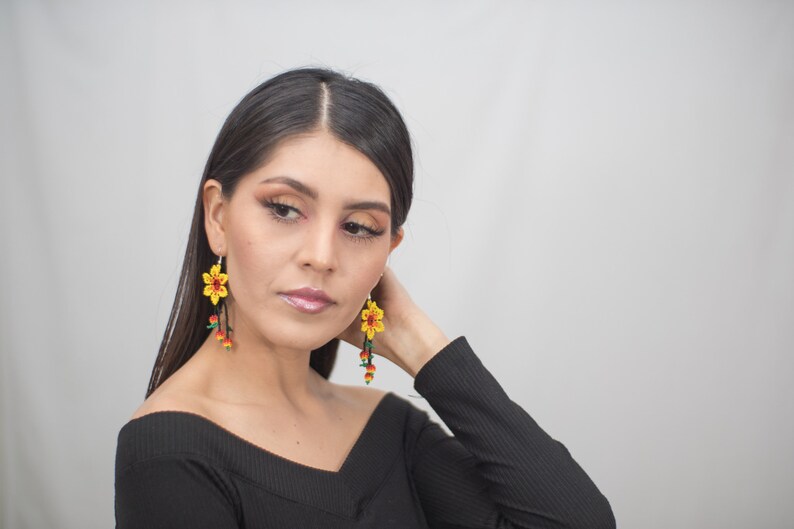 May include: Yellow flower earrings with red and green accents. The earrings have a beaded design and dangle from silver hooks. The floral earrings are a bright and colorful accessory.