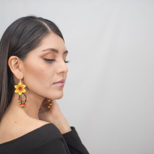 May include: Yellow and red beaded flower earrings with dangling accents. The earrings feature a detailed floral design with a central red bead and yellow petals. The dangling accents include red, yellow, and green beads.