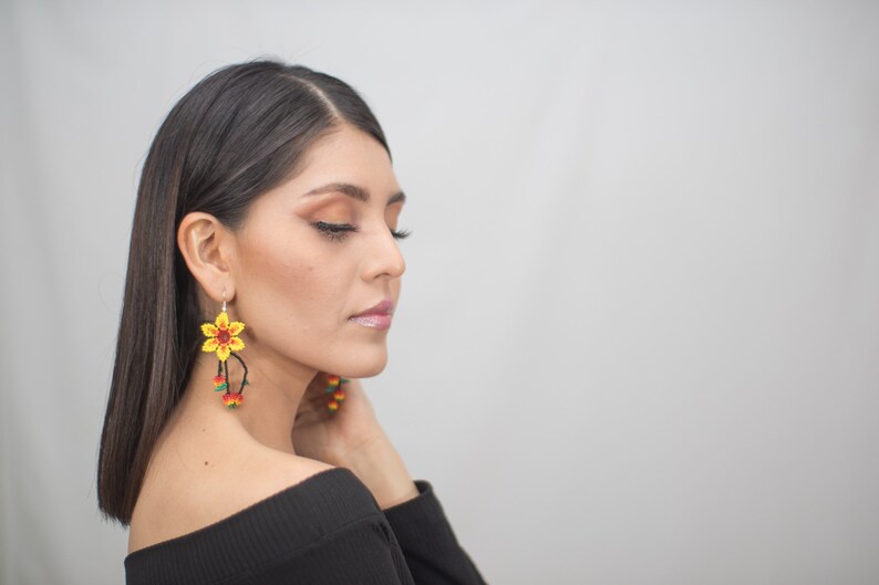 May include: Yellow and red beaded flower earrings with dangling accents. The earrings feature a detailed floral design with a central red bead and yellow petals. The dangling accents include red, yellow, and green beads.