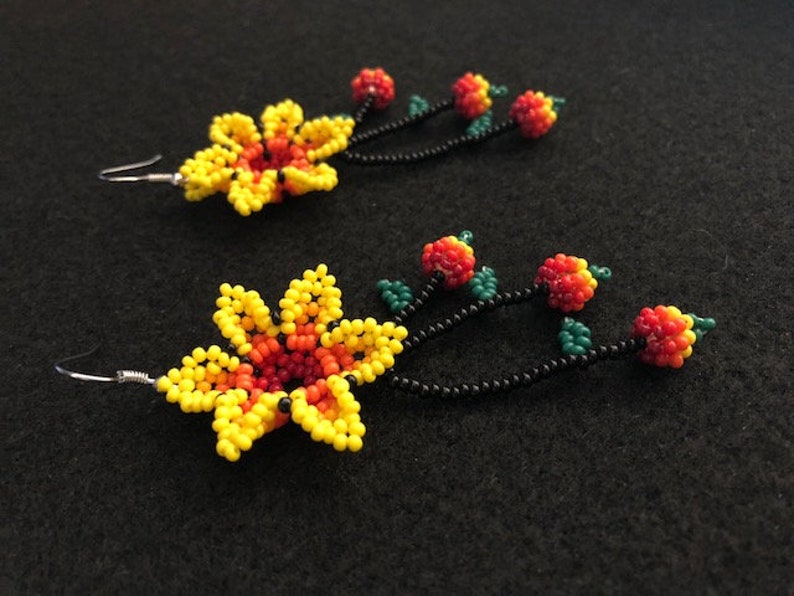 May include: A pair of beaded earrings featuring a yellow and orange flower design with a black stem and red and orange beaded berries. The earrings have silver-colored ear wires and are set against a black background.