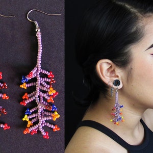 May include: A pair of long, beaded earrings with a purple base and colorful accents. The earrings are shaped like a branch with small, colorful beads clustered together.