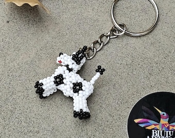 May include: A black and white beaded cow keychain with a silver key ring. The keychain is attached to a black and white sticker with the text "BIUU ARTISAN BOUTIQUE".