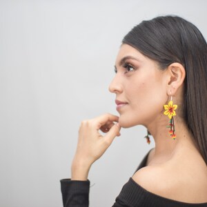 May include: Yellow beaded flower earrings with red and green accents. The earrings have a long, dangling design. The floral earrings are a unique accessory.
