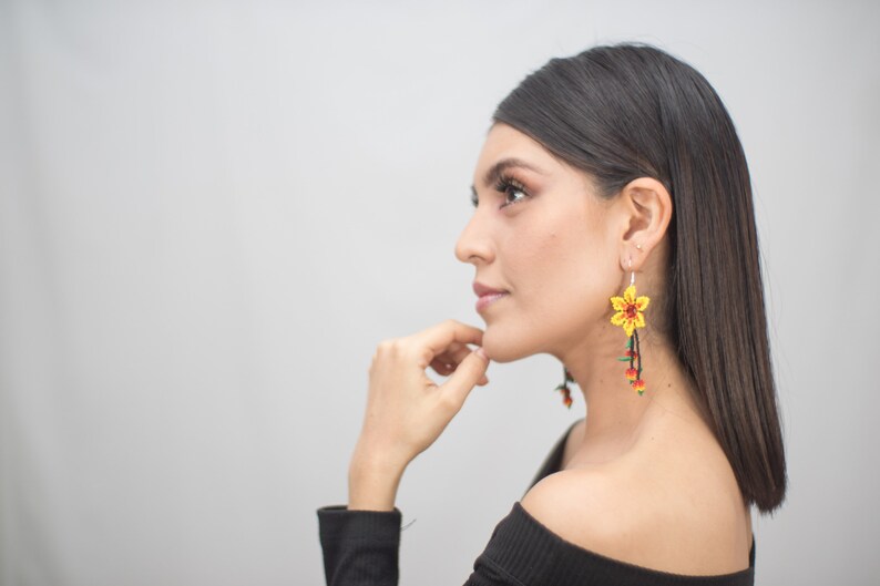 May include: Yellow beaded flower earrings with red and green accents. The earrings have a long, dangling design. The floral earrings are a unique accessory.