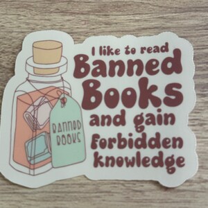 May include: A sticker with a jar illustration and the text "I like to read Banned Books and gain forbidden knowledge." The jar has a cork lid and a tag that says "Banned Books."
