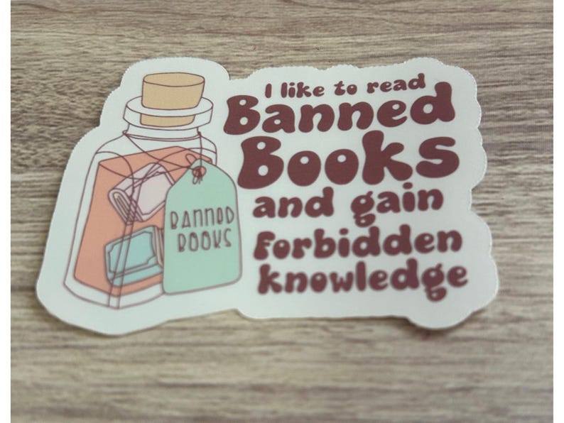 May include: A sticker with a jar illustration containing books and a tag that says "Banned Books." The sticker has text that reads "I like to read Banned Books and gain forbidden knowledge."