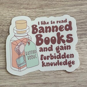 May include: A sticker featuring a potion bottle with a cork stopper and a tag that reads "Banned Books." The sticker has text that says "I like to read Banned Books and gain Forbidden knowledge."