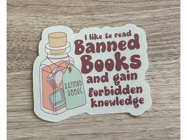 May include: A sticker featuring a potion bottle with a cork stopper and a tag that reads "Banned Books." The sticker has text that says "I like to read Banned Books and gain Forbidden knowledge."