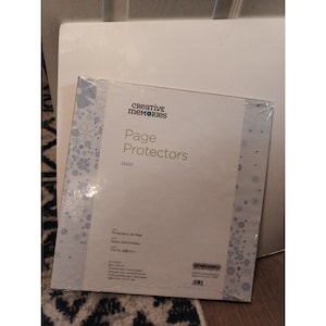 May include: A package of Creative Memories 12x12 inch page protectors. The clear plastic packaging displays the product name and brand logo. The protectors are designed to safeguard scrapbook pages.