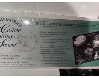 Pode incluir: Uma caixa do Sistema de Corte Personalizado Creative Memories. A caixa apresenta texto em inglês e espanhol, com as palavras "The Creative Memories Collection" em destaque. Inclui informações sobre padrões de corte e acessórios.