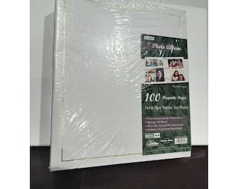 Pode incluir: Um álbum de fotos branco com borda dourada, embalado em plástico transparente. A capa do álbum apresenta o texto "Photo Album" e "100 Magnetic Pages". O álbum foi projetado para fotos de tamanho padrão.