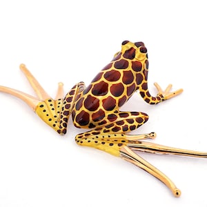 May include: A glass frog figurine with a brown and gold spotted pattern. The frog is sitting on its hind legs with its front legs extended forward. The figurine is made of glass and has a glossy finish.