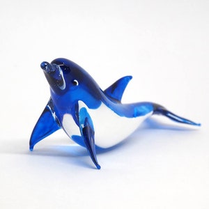 May include: A blue and white glass dolphin figurine. The dolphin is swimming with its head tilted up and its mouth open.