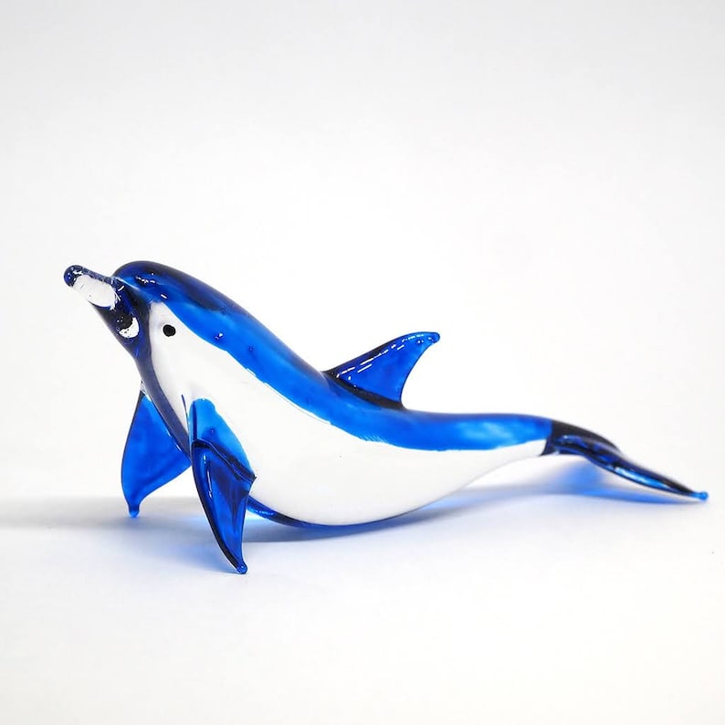 May include: A blue and white glass dolphin figurine. The dolphin is swimming with its mouth open and its tail fin extended.