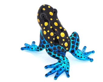 May include: A blue and black glass frog figurine with yellow spots. The frog is sitting on a white surface.