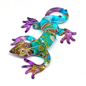 May include: A colorful glass lizard figurine with purple, blue, green, gold, and orange accents. The lizard is posed in a walking position with its tail curled up.