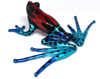 May include: A glass frog figurine with a red, black, and blue color scheme. The frog has black spots on its blue legs and a red and black pattern on its back.