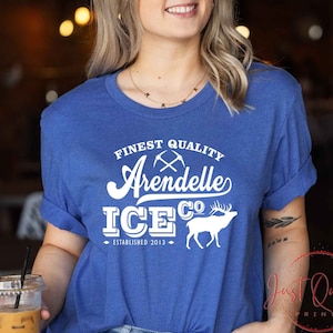 Puede incluir: Una camiseta azul real con texto blanco que dice "Finest Quality Arendelle Ice Co. Established 2013". El texto est&aacute; en una fuente de estilo vintage e incluye un gr&aacute;fico de picos cruzados y una silueta blanca de un ciervo.