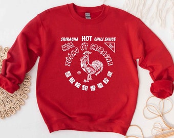 May include: Red sweatshirt with a white graphic of a Sriracha hot chili sauce bottle featuring a rooster and the text "Sriracha Hot Chili Sauce" and "TƯỞNG ỚT SRIRACHA".