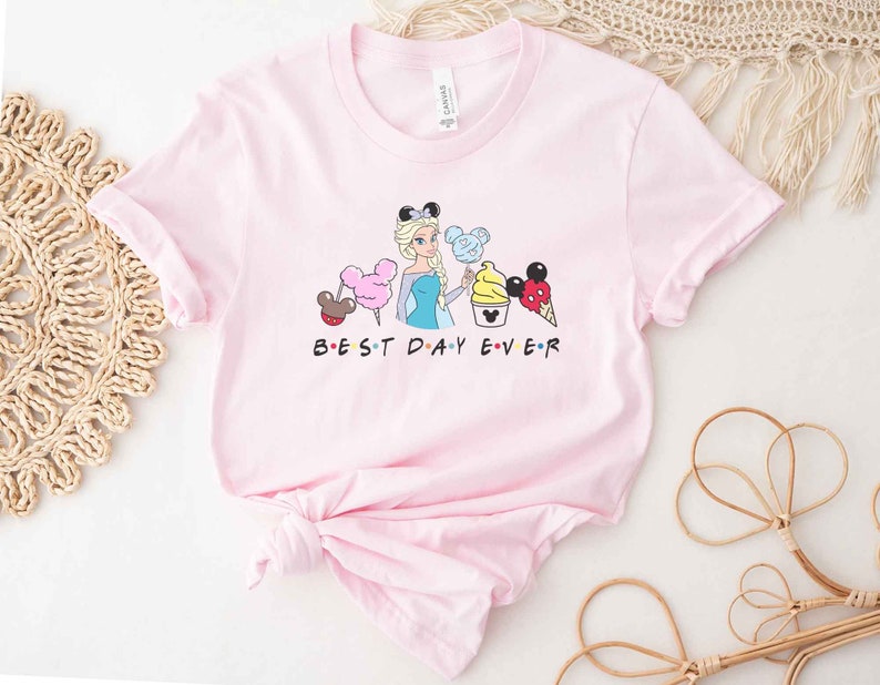 May include: Pink t-shirt with a graphic of a Disney princess character holding a Mickey Mouse ice cream cone and other Disney-themed treats. The text "BEST DAY EVER" is printed below the graphic.