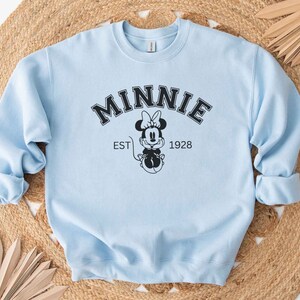 May include: Light blue sweatshirt with a black graphic of Minnie Mouse and the text "MINNIE EST 1928"