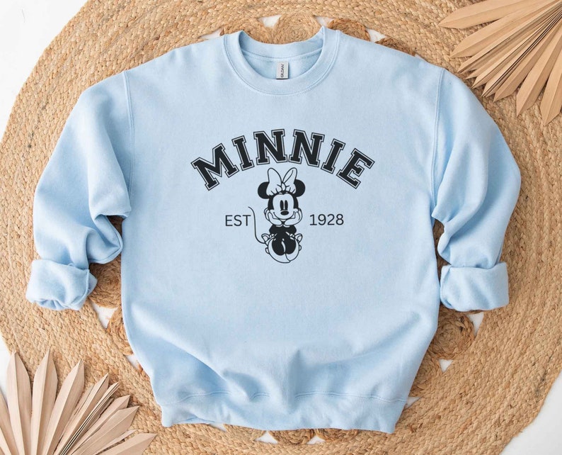 May include: Light blue sweatshirt with a black graphic of Minnie Mouse and the text "MINNIE EST 1928"