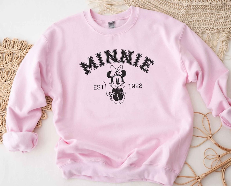 May include: Pink sweatshirt with a black graphic of Minnie Mouse and the text "MINNIE EST 1928"
