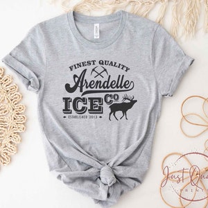 Puede incluir: Camiseta gris con texto negro que dice "Finest Quality Arendelle Ice Co. Established 2013" y una silueta negra de un ciervo.