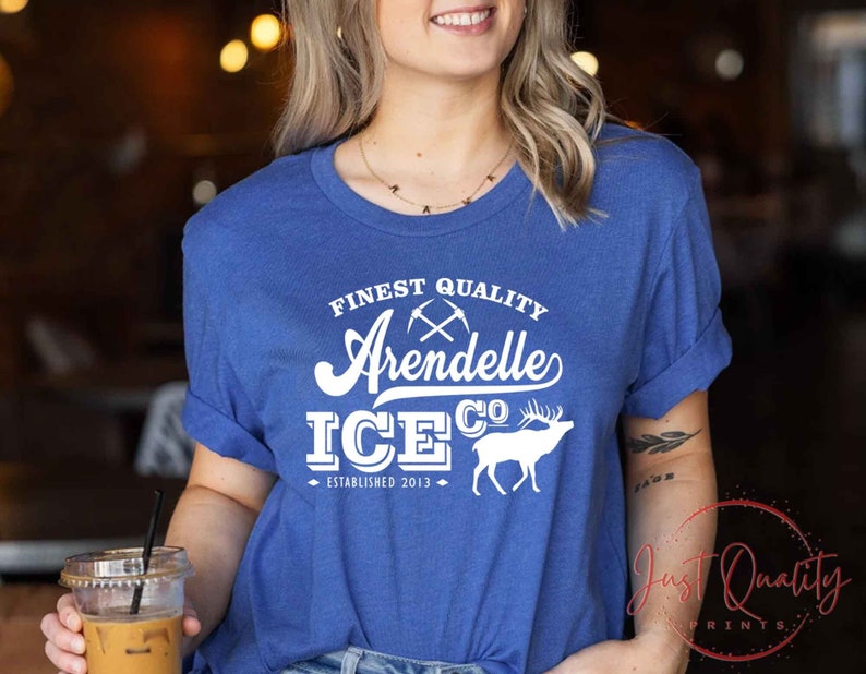 Puede incluir: Una camiseta azul real con texto blanco que dice "Finest Quality Arendelle Ice Co. Established 2013". El texto est&aacute; en una fuente de estilo vintage e incluye un gr&aacute;fico de picos cruzados y una silueta blanca de un ciervo.