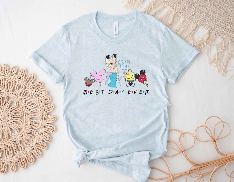 May include: Light blue t-shirt with a graphic of a Disney princess holding a Mickey Mouse ice cream cone and other Disney treats. The text "BEST DAY EVER" is printed below the graphic.