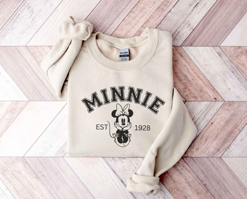 May include: A beige sweatshirt with a black graphic of Minnie Mouse and the text "MINNIE EST 1928".