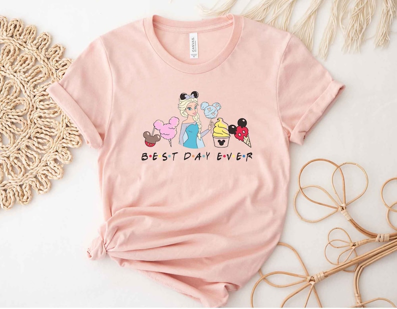 May include: A pink t-shirt with a graphic of a Disney princess holding a Mickey Mouse ice cream cone and other Disney treats. The text "BEST DAY EVER" is printed below the graphic.