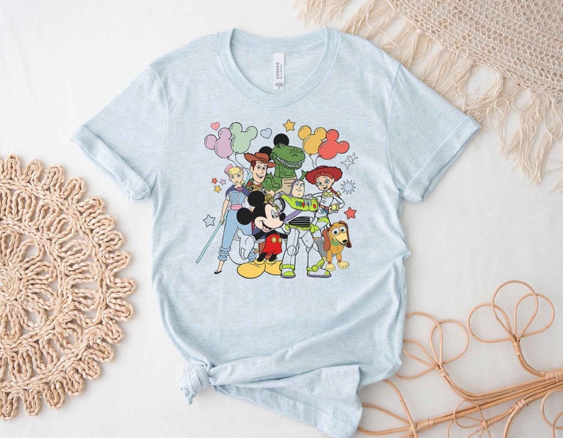 Puede incluir: Camiseta azul claro con un estampado gr&aacute;fico de Mickey Mouse, Woody, Buzz Lightyear, Jessie, Rex y Slinky Dog. Los personajes est&aacute;n rodeados de globos y estrellas de colores.