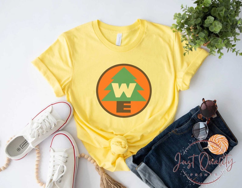 May include: Yellow t-shirt with a green pine tree and the letters "W" and "E" inside a circle. The circle is orange with a brown outline.
