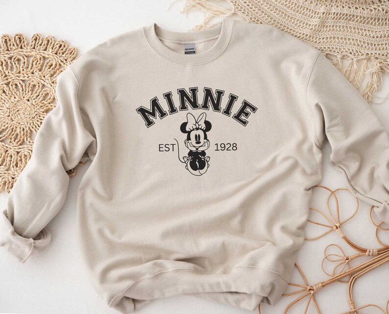 May include: A beige sweatshirt with a black graphic of Minnie Mouse and the text "MINNIE EST 1928".
